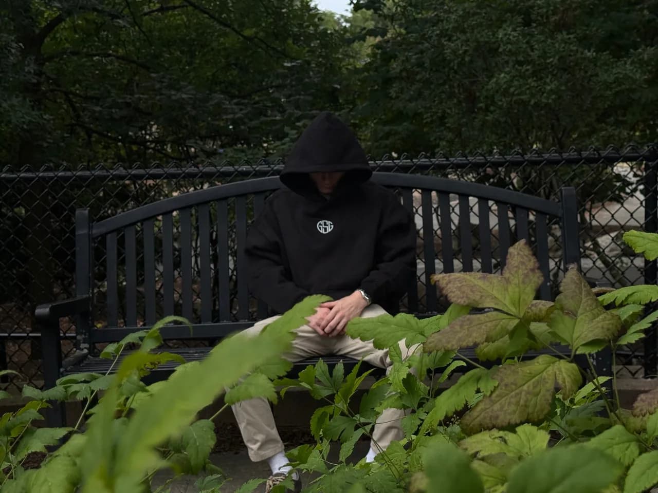 Lifter in a black Grim Street Gym hoodie sitting head down on a park bench